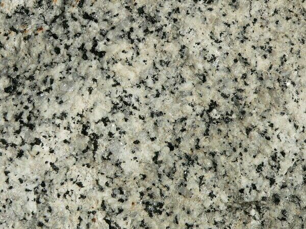 A closeup view of granite, a rock.  It is composite of small grains of the minerals quartz (white) and feldspar (black).  These mineral grains would also be considered crystals.  This would granite would also be considered a stone, particularly when it was going to be carved or used as a building material.